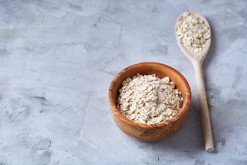 Oat flakes in bowl and wooden spoon isolated on wooden background, close-up, top view, selective focus.