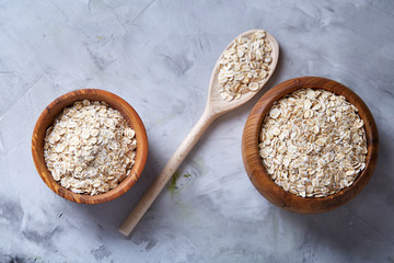 Oat flakes in bowl and wooden spoon isolated on wooden background, close-up, top view, selective focus.