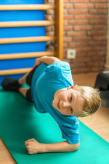 Kind bei der Kinderphysiotherapie macht einen Seitstütz auf einer Gymnastikmatte