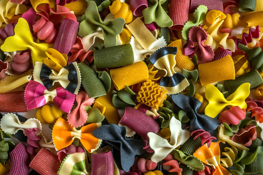 Mixed selection of dried pasta on wooden background. Macaroni scattered on a glass jar. Close up.