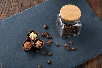 Side view of overturned glass jar with coffee beans and chocolate candies on wooden background,...