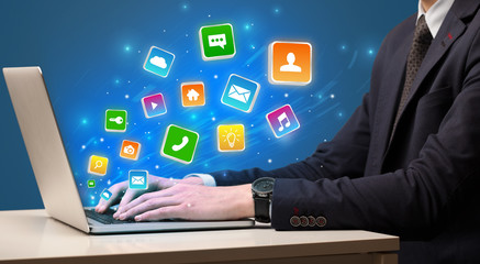Businessman hand typing on laptop with flying application icons around