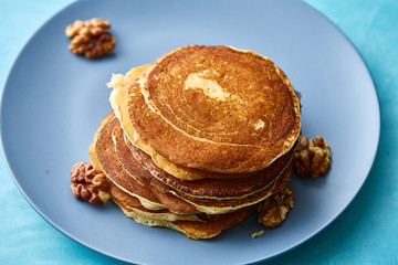 Pile of homemade pancakes with walnuts on blueish plate over blue background, selective focus