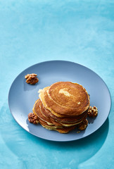Pile of homemade pancakes with walnuts on blueish plate over blue background, selective focus