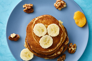 Pile of homemade pancakes with walnuts on blueish plate over blue background, selective focus