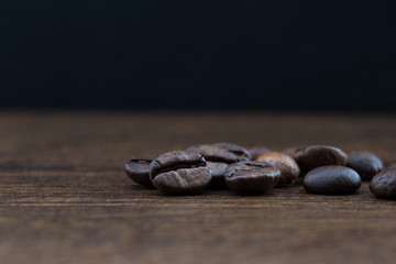 Fototapeta premium Coffee beans on a dark background and a wooden table. Closeup.