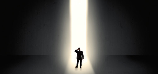 Businessman standing and seeing the light at the end of a big wall
