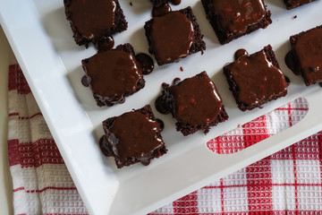Chocolate brownies covered with chocolate nut ganache - Close up top view of brownie squares in white tray
