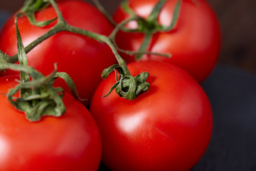 Composition of tomato bunch and hot pepper on black piece of board, top view, close-up.