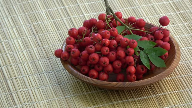 Rotating rowan berries in wooden plate on bamboo mat