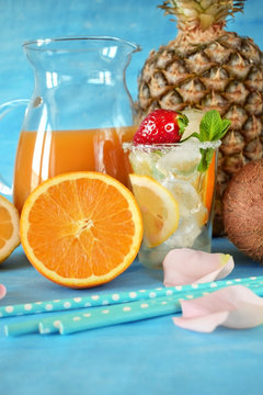 Glass filled up with ice and cocktail ingredients surrounded by orange, lemon, coconut and pineapple