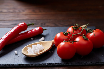 Vegetarian still life with fresh grape tomatoes, pepper and salt in wooden spoon on wooden background, selective focus