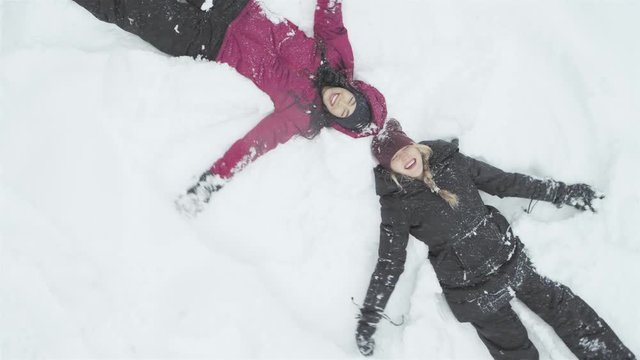 Wide shot of two young beautiful women laying on the snow, and making snow angels