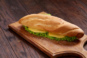 Fresh and tasty sandwich with cheese and vegetables on cutting board over white textured background, selective focus.