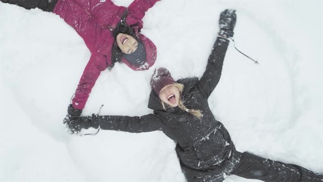 Two young beautiful women laying on the snow, and making snow angels