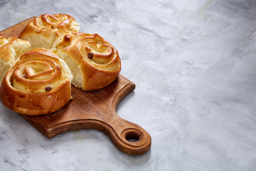 Homemade rose buns on wooden cutting board over white textured background, close-up, shallow depth of field