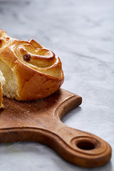 Homemade rose buns on wooden cutting board over white textured background, close-up, shallow depth of field
