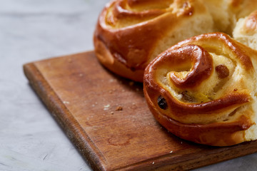 Homemade rose buns on wooden cutting board over white textured background, close-up, shallow depth of field