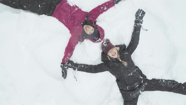Two young beautiful women laying on the snow, and making snow angels