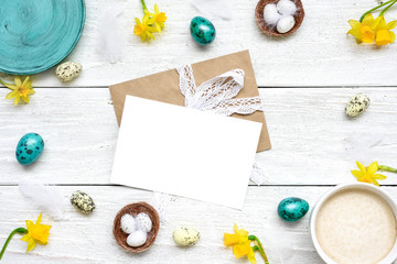 easter greeting card in frame made of quail eggs, cup of cappuccino and spring flowers on white wooden background