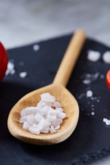 Fresh tomatoes and a spoon of salt on black stony board over white background, close-up, selective focus.