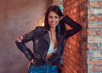 Naklejka premium A happy sexy sensual brunette posing in underwear and stylish leather jacket leaning against a brick wall.