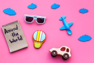 Travelling with child concept. Air balloon, car and plane. Around the world hand lettering in notebook on pink background top view copy space