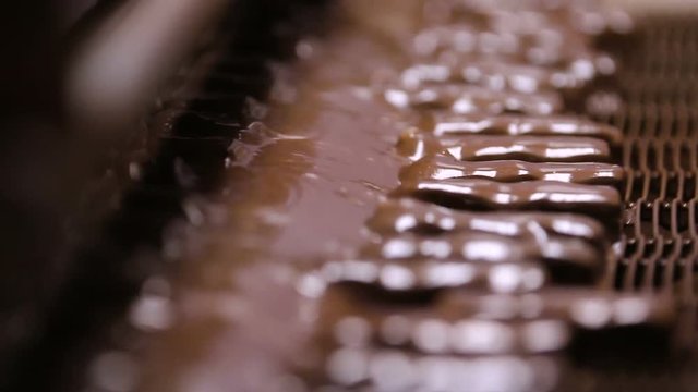 Bars of nougat with nuts are poured with chocolate. Manufacture of chocolate bars with nougat and peanuts. Chocolate bars move along conveyor belt at confectionery factory for the production of sweets