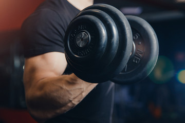 Dumbbell. Close-up of man lifts dumbbell to biceps in gym.