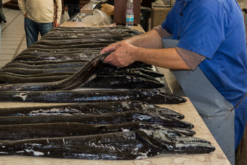 Vendor man arranging black scabbard fishes on the market table. Mercado dos Lavradores in Funchal,...