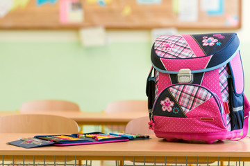 Pink girly school bag and pencil case on a desk in an empty classroom. First day of school concept.