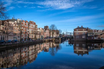 Foto op Plexiglas Kanaal waterkanalen in Amsterdam met blauwe wateren en blauwe lucht op een zonnige dag met een weerspiegeling van traditionele gebouwen in de wateren van het kanaal