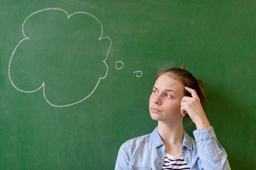 Student thinking blackboard concept. Pensive girl looking at thought bubble on chalkboard...