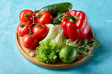 Still life of fresh organic vegetables on wooden plate over blue background, selective focus, close-up