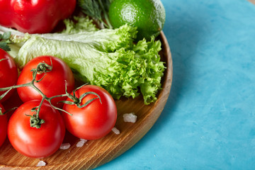 Still life of fresh organic vegetables on wooden plate over blue background, selective focus, close-up