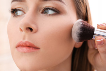 Professional visage artist applying makeup on woman's face in salon, closeup