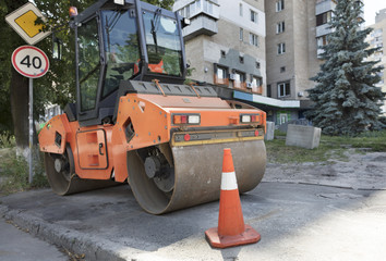 Orange road cone protect heavy wheel compactor along the edge of the city street road