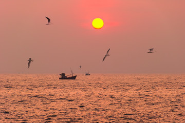 Sea landscape at sunset time with fishing boat on the horizon and birds. Toned in pink color with instaram style.