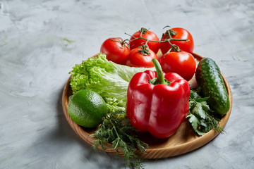 Still life of fresh organic vegetables on wooden plate over white background, selective focus, close-up