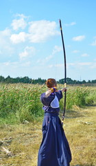Archer. Asian. Young Japanese girl in traditional medieval clothes with long hunting bow and arrow...