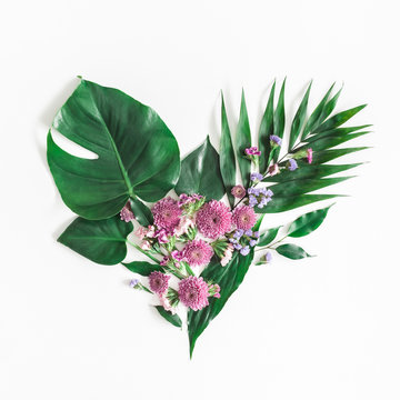 Summer tropical composition. Heart symbol made of green tropical leaves and pink flowers on white background. Summer concept. Flat lay, top view, square