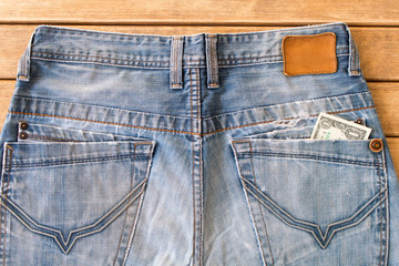 Blue jeans with a dollar in your back pocket on a wooden background . The view from the top