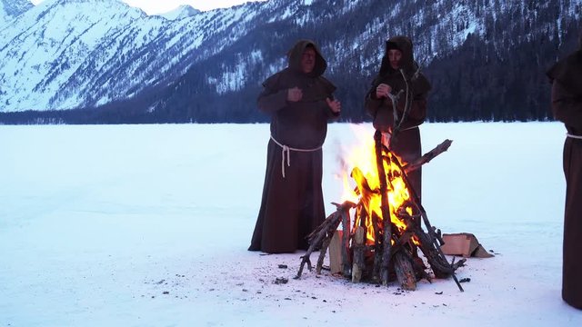 monks franciscans are warming near fire in winter