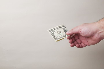 hand giviing one dollar banknote on gray background, copy space