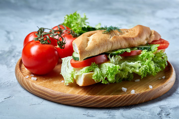 Fresh sandwich with lettuce, tomatoes and cheese served on wooden plate over white textured background, selective focus