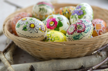 Fototapeta na wymiar Colorful painted Easter eggs in brown wicker basket on branches, traditional Easter still life, painted flowers, wooden nest