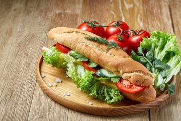 Fresh sandwich with lettuce, tomatoes and cheese served on wooden plate over rustic background, selective focus