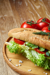 Fresh sandwich with lettuce, tomatoes and cheese served on wooden plate over rustic background, selective focus