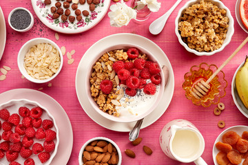 Granola with natural yogurt, fresh raspberries, honey, almond flakes, and poppy seeds in a ceramic bowl on a pink wooden table, top view. Delicious and nutritious breakfast or dessert. Healthy food.