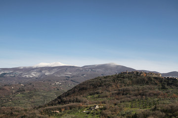 Obraz premium talian Countryside. Tuscany. Daylight. Blue Sky. Spring. Green Hills, a Peaceful Village, a Snowy Mountain in the Background